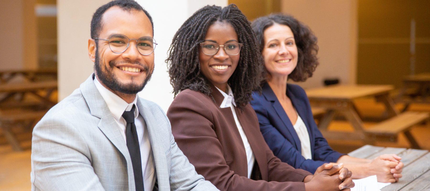 Happy diverse business team posing in street cafe. Business man and women with clasped hands sitting at table outside, looking at camera and smiling. Successful team concept